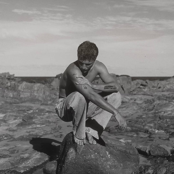 Musician Che Burns in a black and white photo sitting on a rock in Mooloolaba
